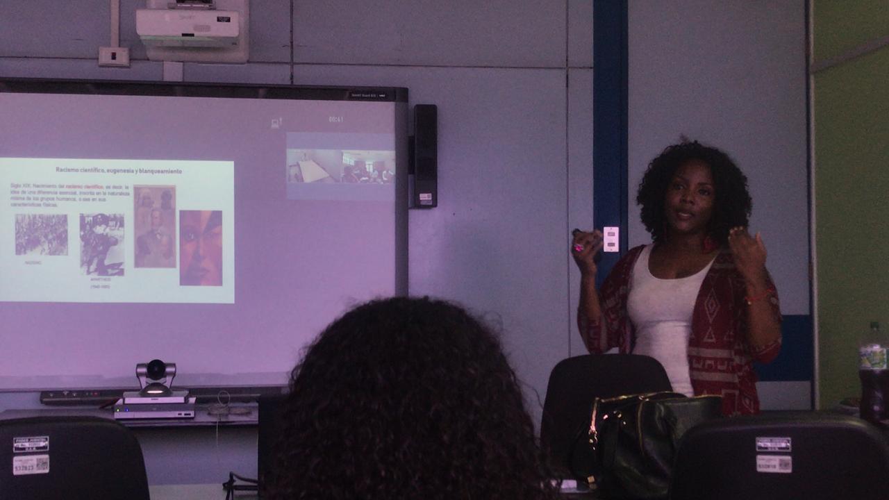 Mujer afrodescendiente exponiendo al frente de la clase 