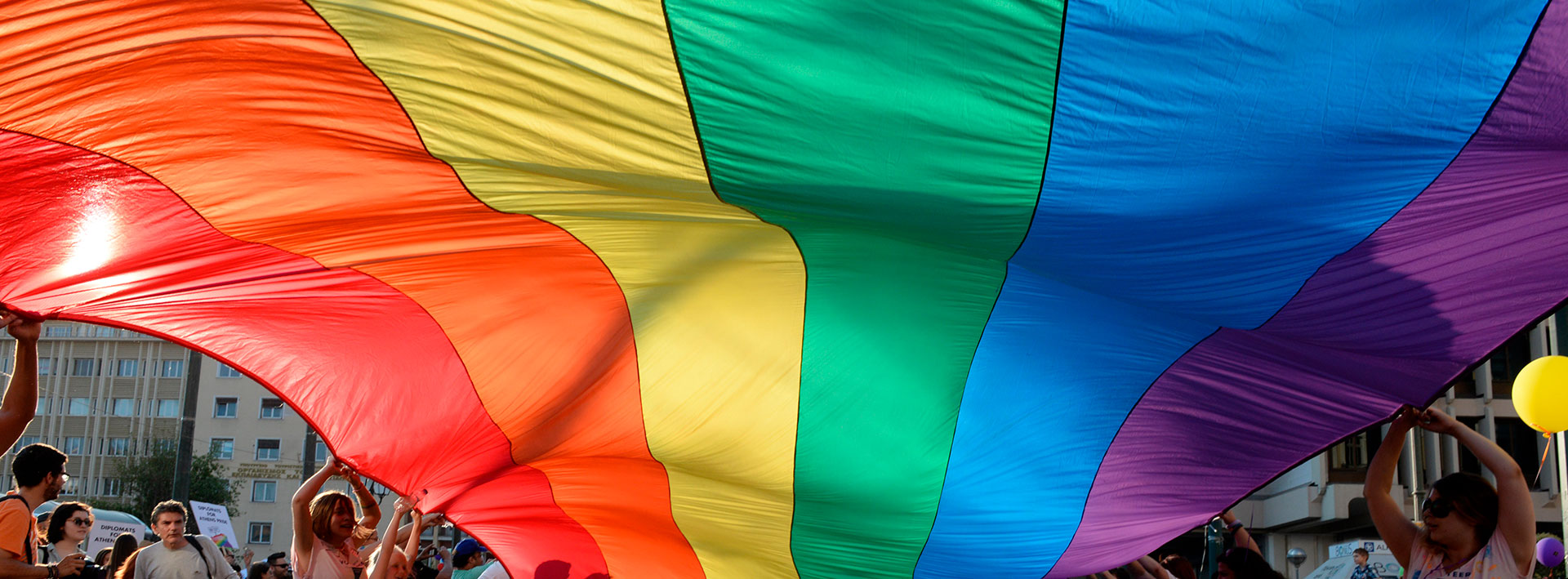Bandera multicolor sostenida por un grupo de personas, representa a la comunidad LGTBIQ